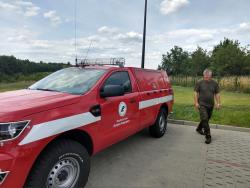 Nowy czerwony samochód terenowy do celów partolowo - gaśniczych. Po prawej stronie uśmiechnięty kierowca ubrany na zielono - 2018 rok